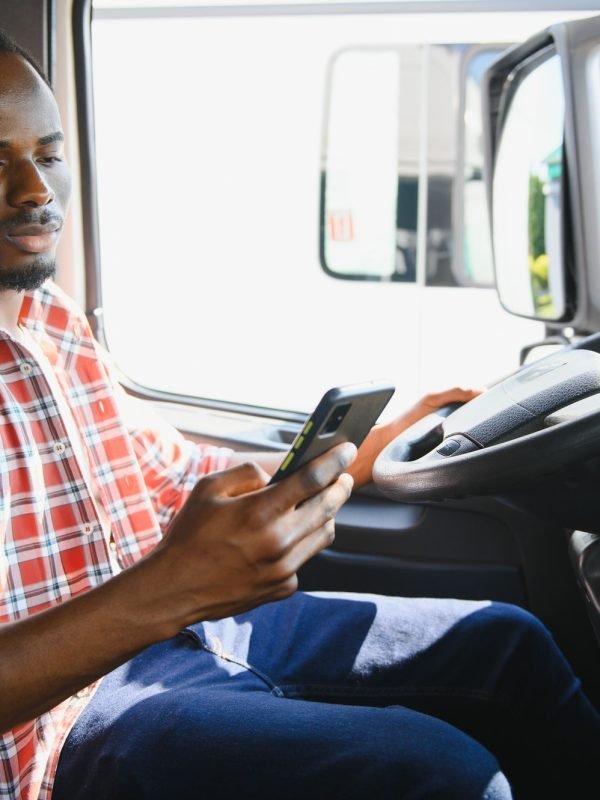 Young african american truck driver using mobile phone while driving transport vehicle.